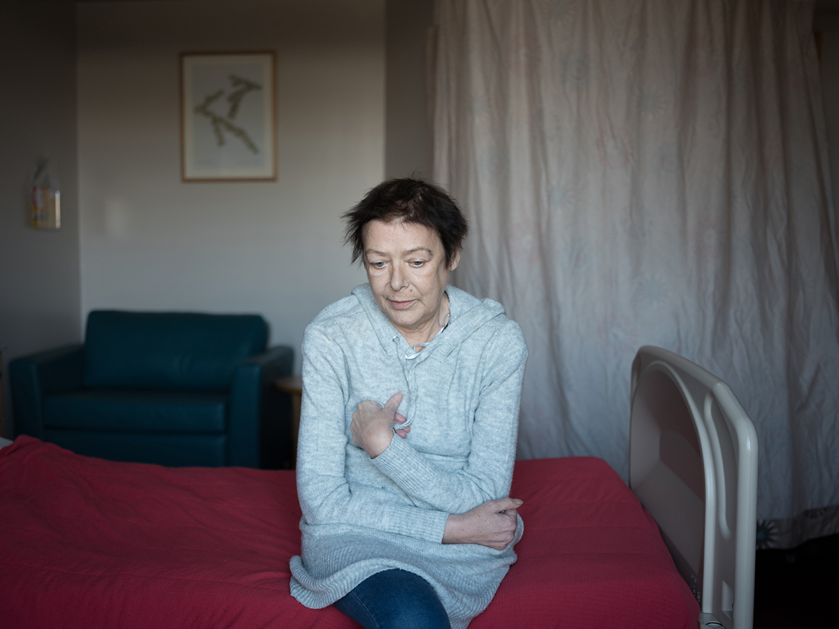 Photograph of a person sat on a bed which appears to be a hospital bed.
