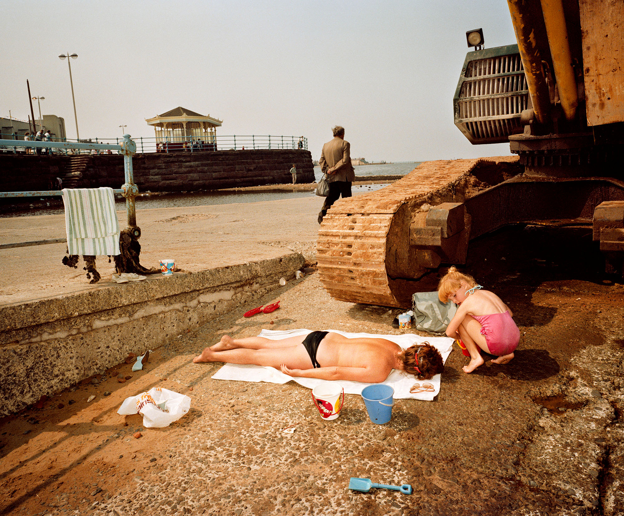 Photographer's image showing New Brighton seafront in 1983-85.  A person laying on a beach towel with an excavator track poised to run over the person.