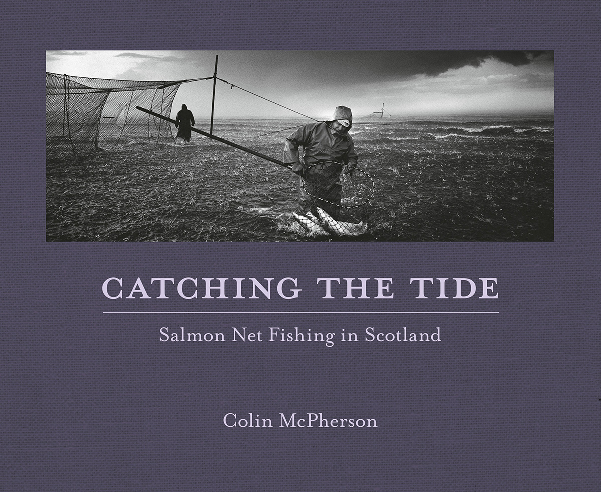 Photographers image of two fishermen working in the rain.  Both are stood in the water.  One holds a net containing a number of large fish.