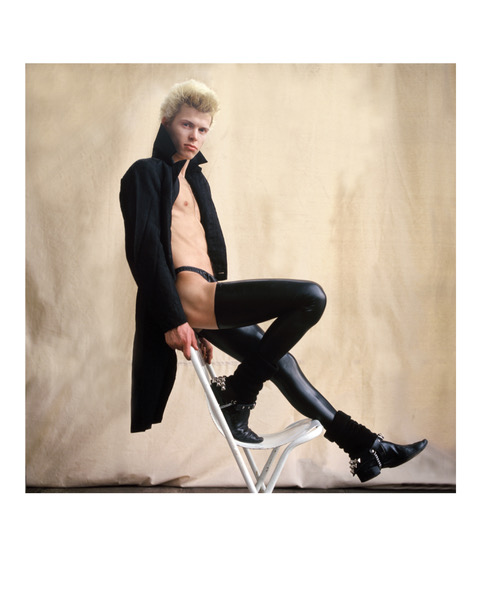 Singer Billy Idol posing on a chair wearing a long black coat