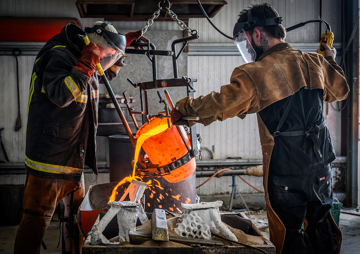Sculptors placing molten metal into a mould.